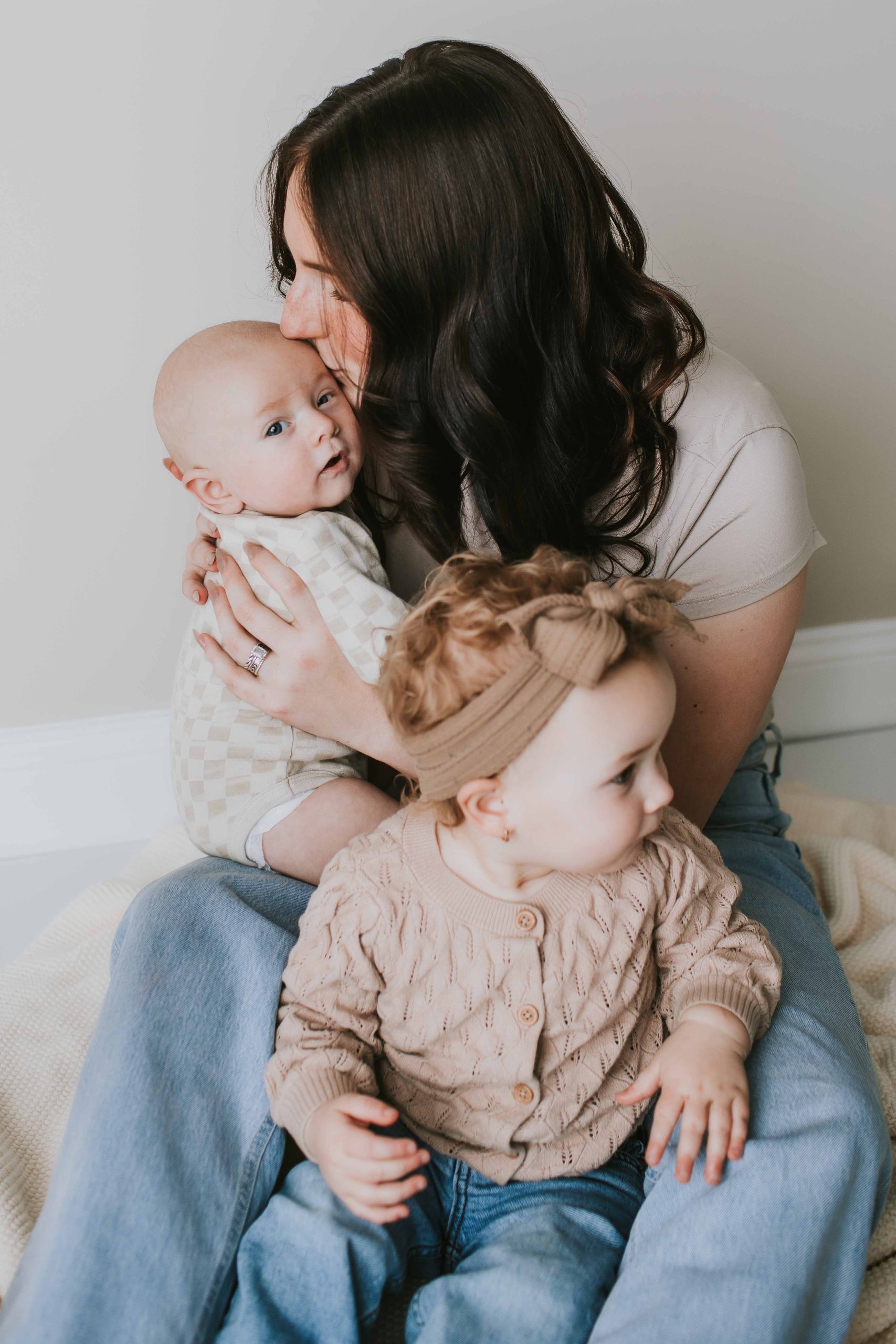 mom kissing newborn with toddler also in her lap