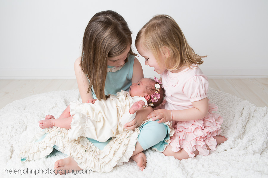Older sisters holding their newborn baby sister