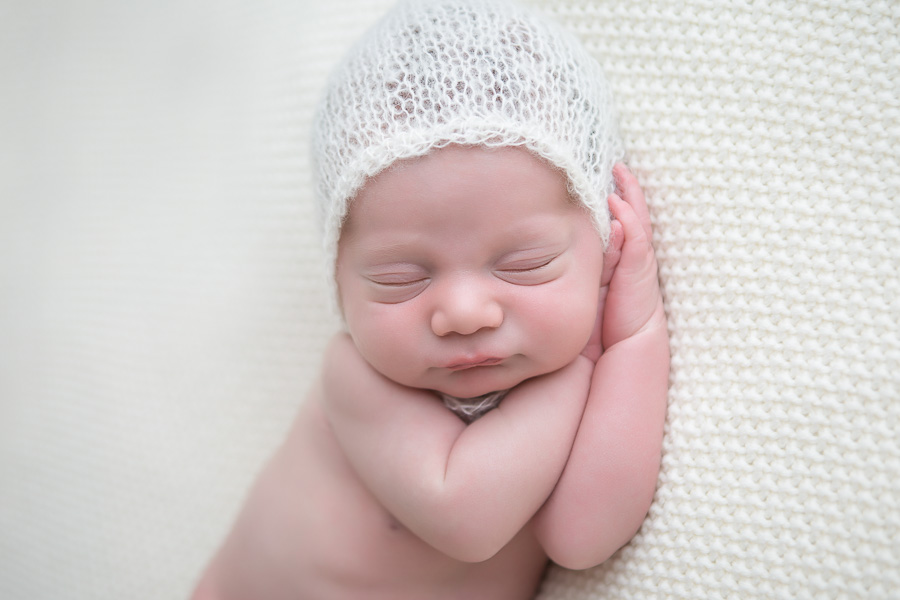 close up of newborn boy sleeping on hands in white mohair bonnet