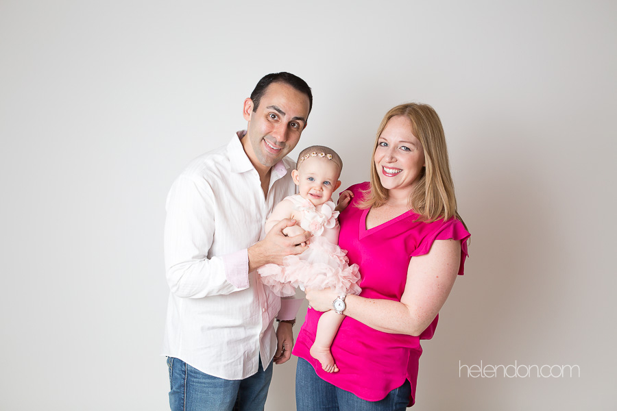 parents smiling holding daughter in white studio