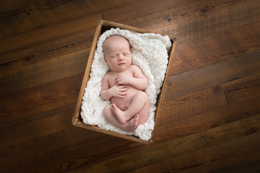newborn boy sleeping in crate on wood floor
