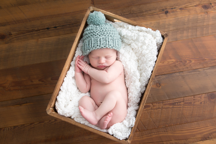 newborn boy sleeping on white blanket in wood box