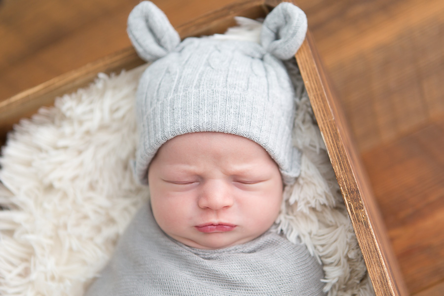 newborn boy making grumpy face in bear hat