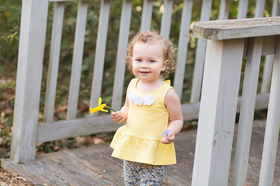 one year old girl holding daffodil laughing
