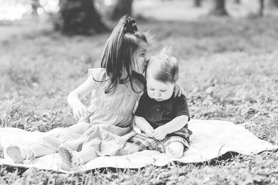 b&w of 3 year old sister kissing baby brother on head
