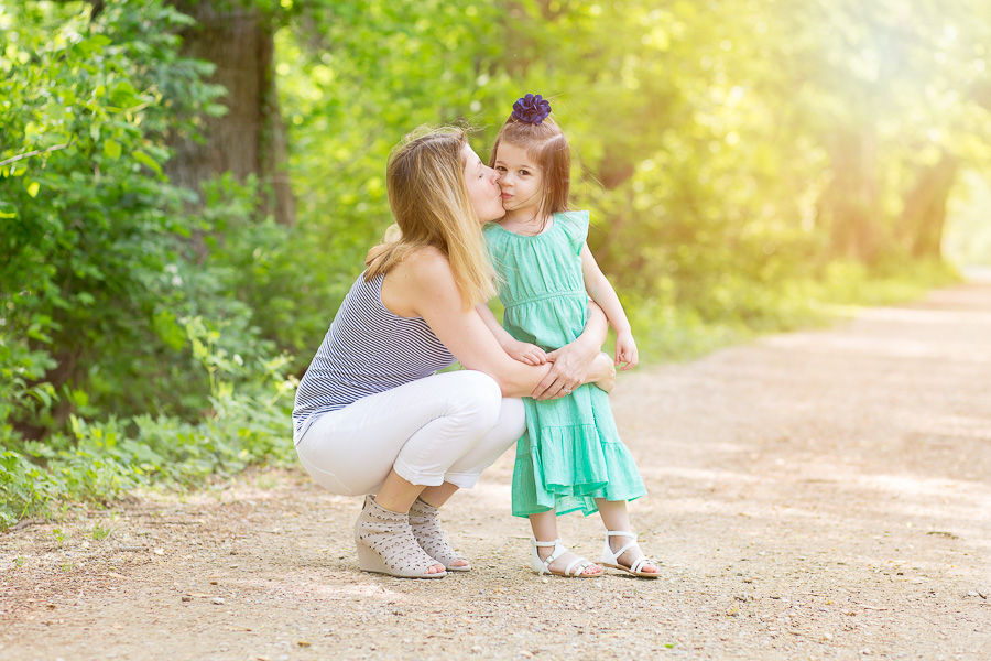 outdoor portrait of mom kissing daughter with sunflare 