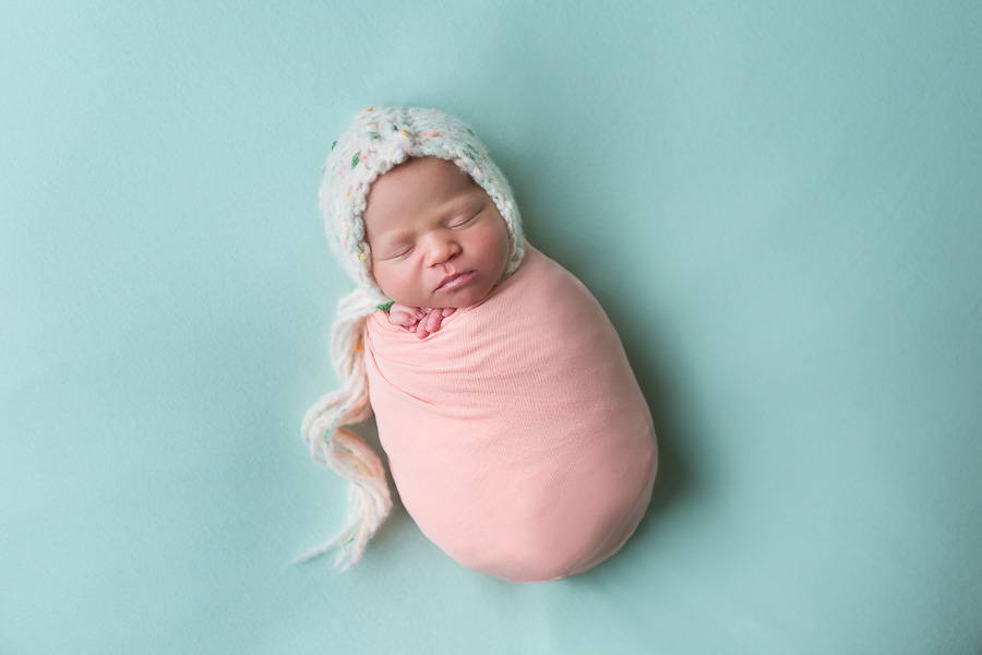 newborn girl swaddled in pink on green blanket