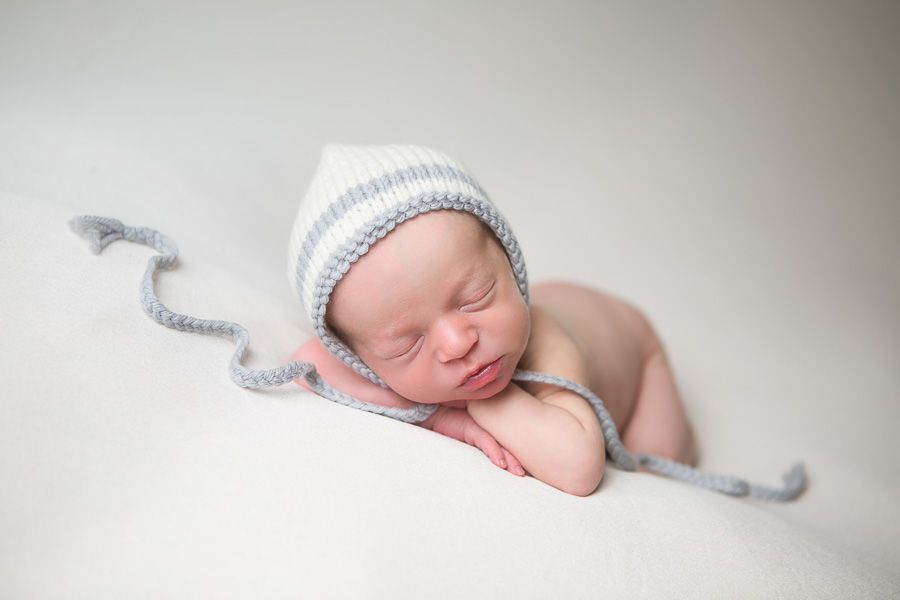 newborn boy in bonnet on white blanket
