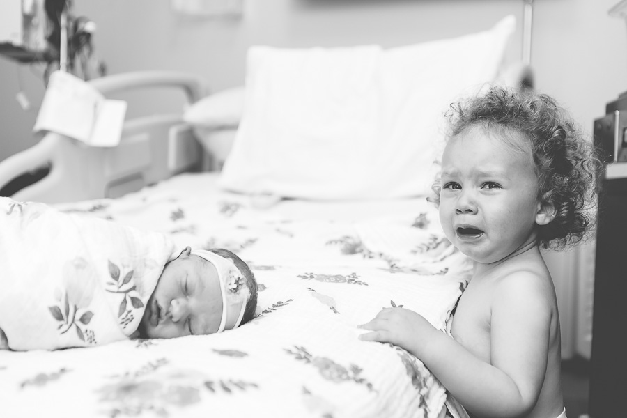 older sister crying next to newborn baby sister at hospital