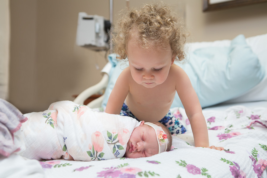 older sibling looking down at newborn sister in hospital