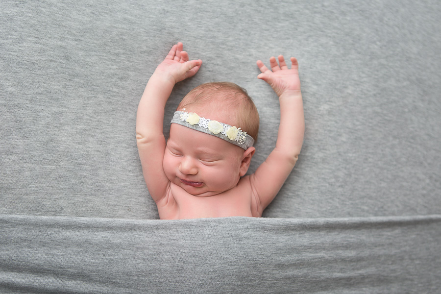 newborn girl on grey blanket stretching