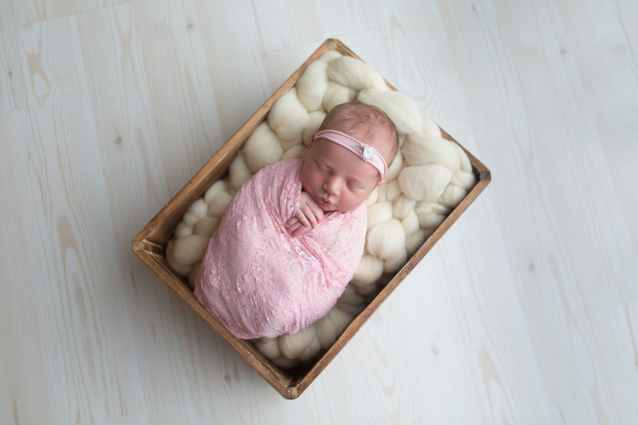 newborn girl sleeping in crate swaddled in pink lace