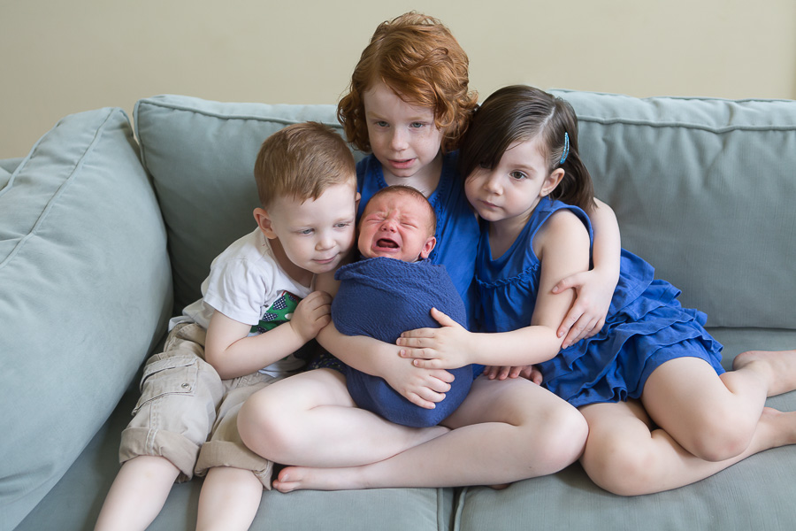older brother and sisters comforting crying newborn baby