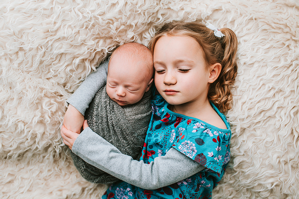five year old sister hugging newborn brother