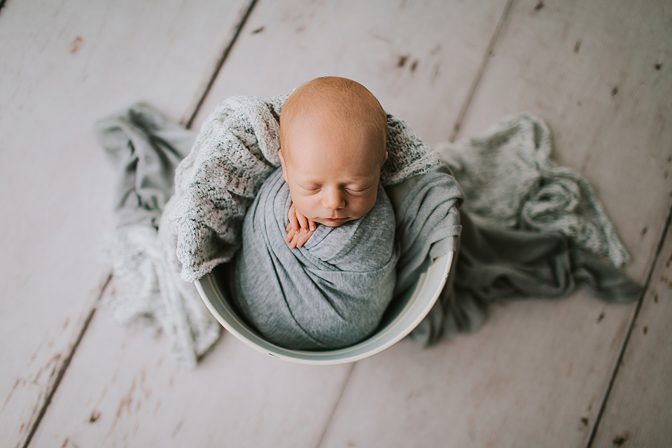 newborn baby boy sleeping swaddled in grey in bucket
