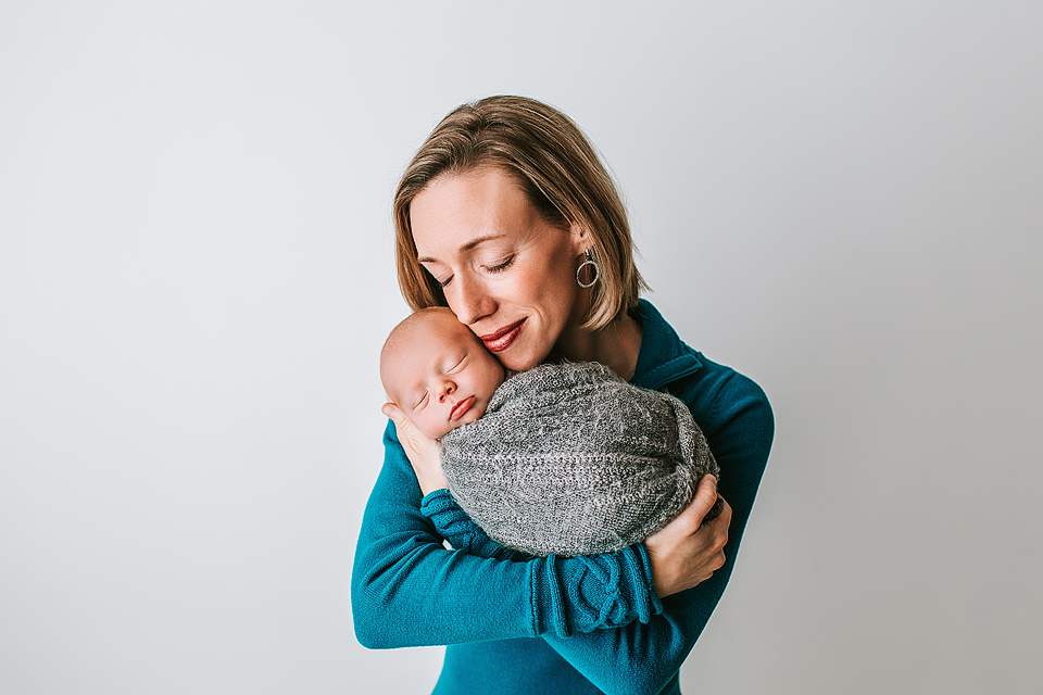 mother holding newborn son smiling with eyes closed